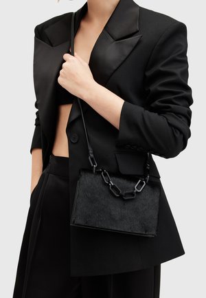 Svart handväska med rektangulär form, texturerad pälsfront och en kraftig kedjestropp. Matchad med en svart blazer i en smäcker design.