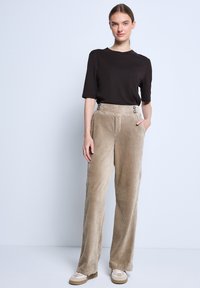 Černé tričko s krátkým rukávem doplněné širokými béžovými kordovým kalhotami s vertikálními pruhy a knoflíkovými detaily v pase.