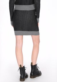 Vestido acanalado en negro y gris con un cuerpo ajustado y dobladillo contrastante, combinado con botines negros de cordones con detalles en amarillo.