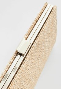Pochette tissée beige avec un fermoir et un cadre en métal argenté, montrée en vue rapprochée inclinée.