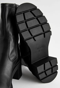 Las botas de tobillo de cuero negro cuentan con una cremallera lateral, una textura suave y una suela de goma gruesa con un patrón de rejilla para mayor tracción.