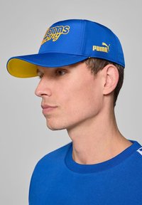 Niebieska czapka z żółtym daszkiem, z napisem "Williams Racing" wyszytym na żółto oraz logo Pumy po boku. Wykonana z gładkiego materiału.