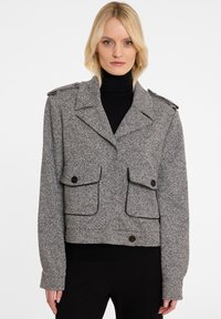 Kraagloze grijs en zwart gespikkelde jas met een brede kraag, schouderepauletten, twee zakken aan de voorkant en knopenaccenten. Textuurstof.