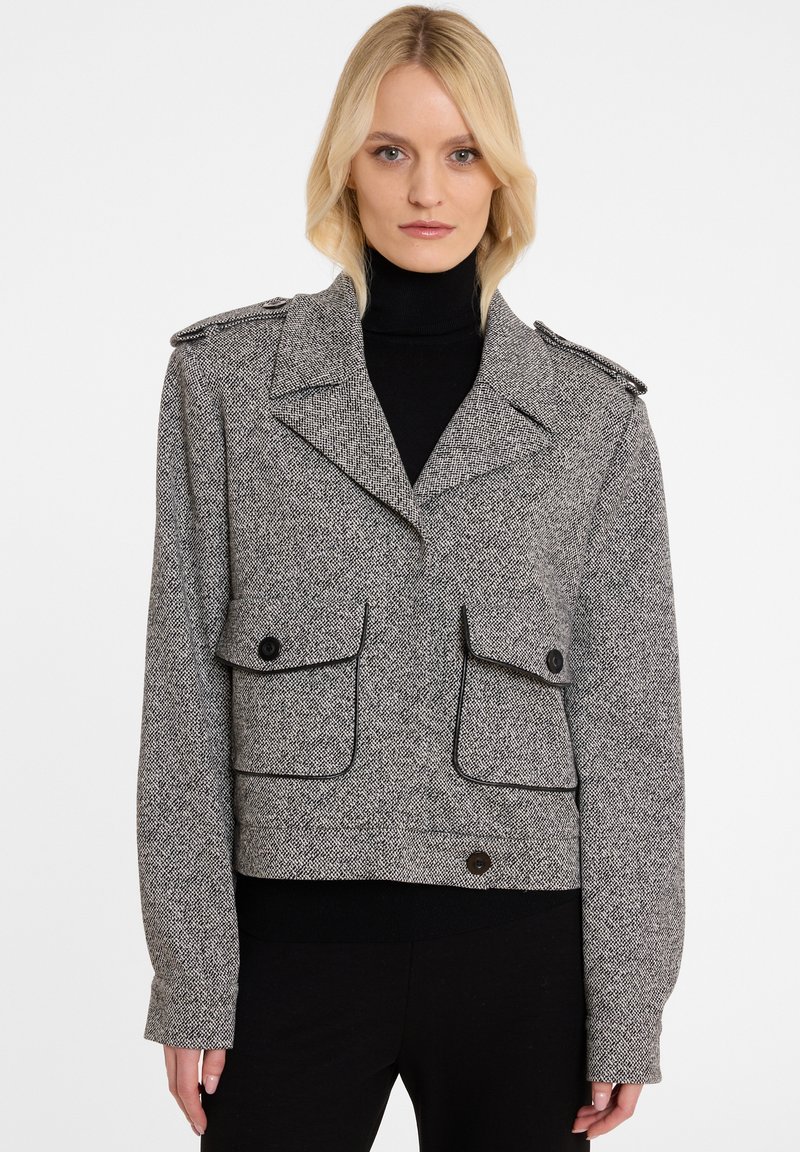 Kraagloze grijs en zwart gespikkelde jas met een brede kraag, schouderepauletten, twee zakken aan de voorkant en knopenaccenten. Textuurstof.