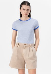 T-shirt rayé bleu et blanc à manches courtes avec un ourlet bleu. Associé à un short beige plissé avec des poches latérales et un détail de bouton.