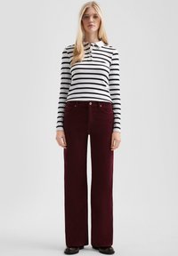 Gestreepte lange mouwen polo in zwart en wit, gecombineerd met bordeauxrode corduroy wijde broek. Voorzien van een knoopsluiting bij de kraag en zijzakken.