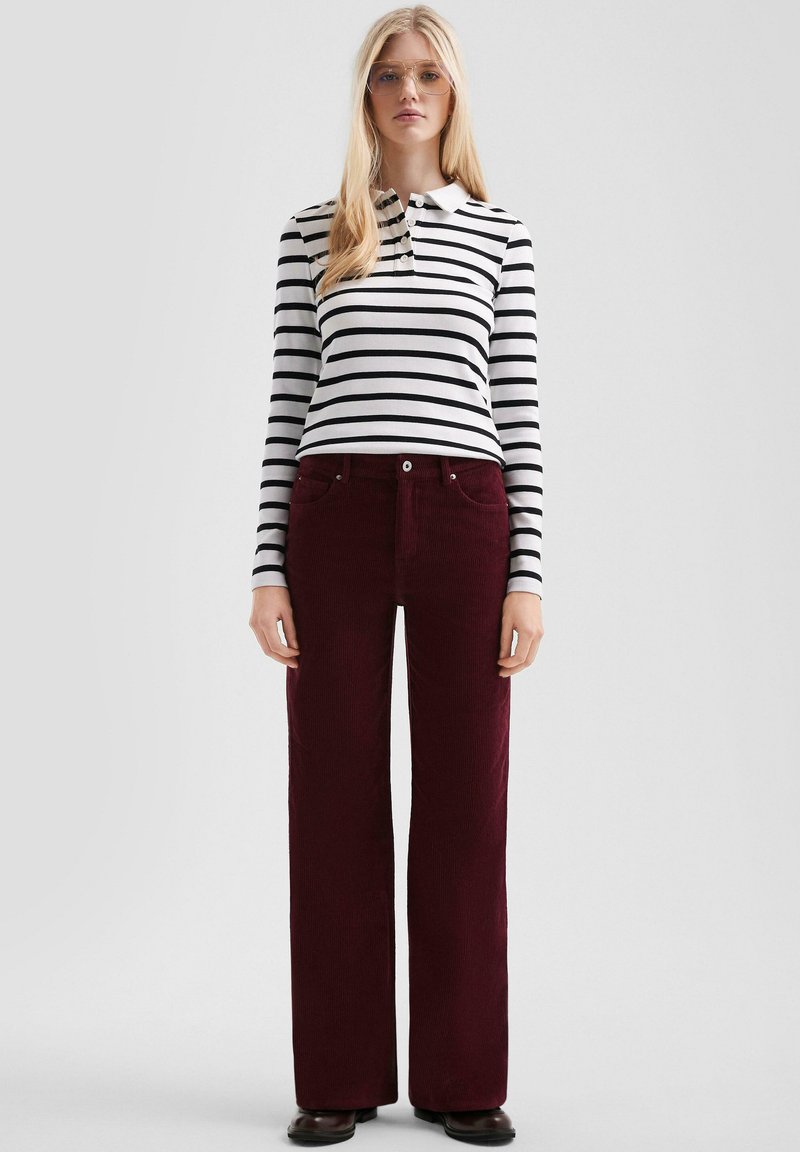 Gestreepte lange mouwen polo in zwart en wit, gecombineerd met bordeauxrode corduroy wijde broek. Voorzien van een knoopsluiting bij de kraag en zijzakken.