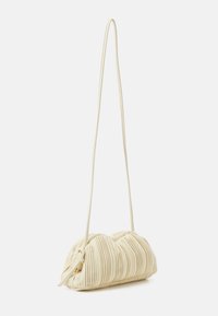 Zmačkaná krémová kabelka s hladkým povrchem a dlouhým tenkým popruhem. Má zaoblený tvar a skládací design.