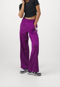 Purple jogger pants with a relaxed fit, elastic waistband, and side pockets. Features white accents and Nike logo on the left leg.