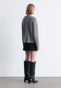 Helle graue gestrickte Sweater mit lockerer Passform, schwarzer Minirock und kniehoche schwarze Stiefel aus Krokodillederimitat mit Blockabsatz.