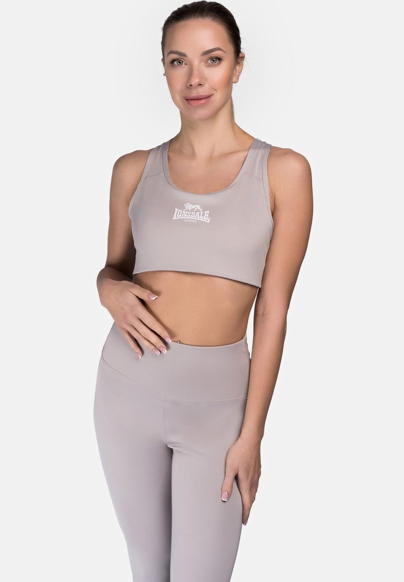 Šviesiai pilkas sportinis liemenukas su lygiu paviršiumi ir Lonsdale logotipu, derinamas su atitinkančiomis aukštai juosmeninėmis leggingais. Tinka sportinei aprangai.