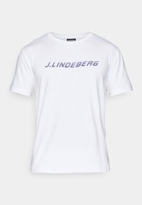 Balta medvilnės marškinėliai su trumpomis rankovėmis ir apvalia kaklo išpjova, ant krūtinės išryškinta mėlyna logotipo užrašas "J. Lindeberg" drąsiu, įstrižiniu stiliumi.
