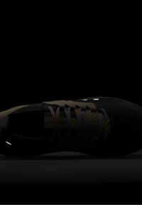 Chaussure de sport noire avec tige texturée, plusieurs lacets et petits points réfléchissants sur le côté, vue de dessus sur fond sombre.