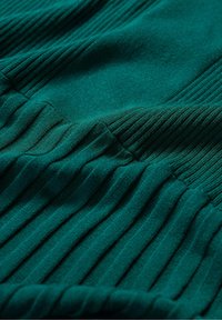 Textured green fabric with ribbed patterns, featuring vertical lines and soft knit. Focus on the velvety surface and elastic edges.