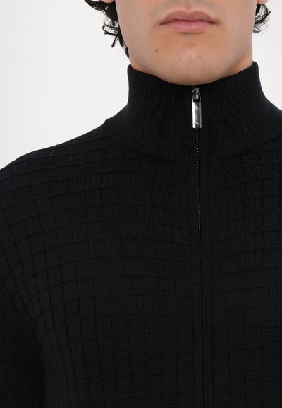 Pulover negru cu fermoar, cu guler înalt, ce prezintă un model texturat de pătrățele mici și un sistem de închidere cu fermoar argintiu.