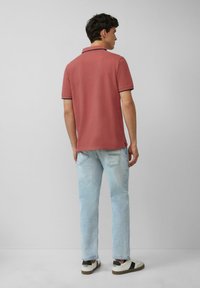 Polo in rosa polveroso con colletto a contrasto, abbinato a jeans azzurri chiari. L'outfit presenta sneakers casual con dettagli neri.