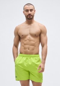 Bañador corto de color verde lima con cintura elástica y bolsillos laterales, confeccionado con material de secado rápido, y con un pequeño logo en el dobladillo.