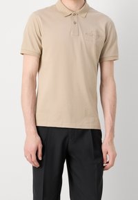 Beige kortærmet polo-shirt med spids krave, tre-knap knaplukning og broderet logo detalje på venstre bryst.
