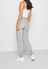 Grå sweatpants med elastiskt midjeband och mudd vid anklarna, med sidfickor och subtil logotypdetaljering. Bärs med en vit tanktop och sneakers.