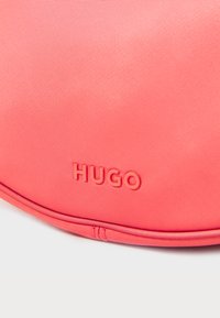 Borsa rosa in nylon con superficie testurizzata; presenta il logo "HUGO" in rilievo. Forma arrotondata e dettagli cuciti lungo i bordi.