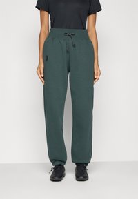 Grønne fleece joggebukser med elastisk midje og snor. Har sidelommer og en liten logodetalj på venstre lår.