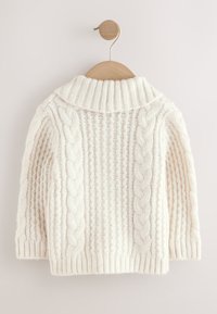 Pull en maille torsadée couleur crème avec col roulé, manches longues et texture côtelée épaisse, suspendu à un cintre en bois sur un fond neutre.