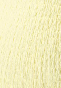 Tecido texturizado e leve numa cor amarelo pastel com padrões ondulados por todo o lado, criando uma superfície tátil subtil.