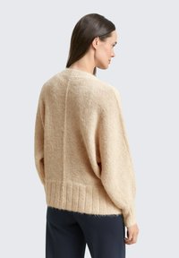 Beżowy dziany sweter o luźnym kroju, z prążkowanym dołem, szerokimi rękawami i miękką teksturą. Widok od tyłu ukazuje szew wzdłuż kręgosłupa.