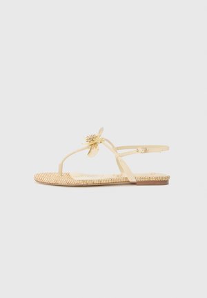 Sandales plates beige avec un accent floral, des brides translucides et une semelle tissée texturée. Design minimaliste adapté aux temps chauds.