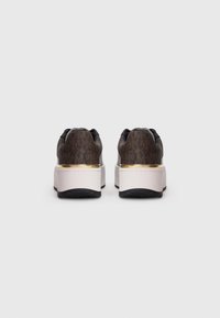Et par brune mønstrede platform sneakers med guldkanter og tykke hvide såler set fra bagpå på en ensfarvet hvid baggrund.