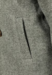 Hallhallane kasukas, millel on horisontaalne küljetasku puhta lõikega. Tekstuur on pehme ja sellel on veidi karvane pind.