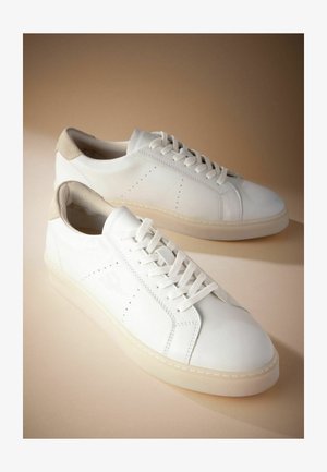 Tenisi din piele albă cu o tabără de călcâie din suede bej texturat. Au un design cu șireturi, perforații minime și o talpă groasă, translucidă.