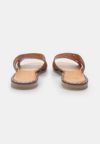 Sandali in pelle marrone caratterizzati da due cinturini curvi con design a intaglio. La soletta è liscia e piatta, arricchita da un bordo cucito.