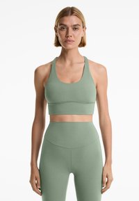 Ljusgrön tränings-bh och högmidjade leggings, båda i ett slätt material. Bh:n har en rundad halsringning och breda axelband, med minimala sömmar.