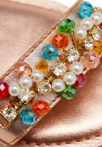 Chancla deslizante en oro rosa con una correa adornada con cuentas coloridas, cristales y perlas sintéticas de diversas formas y tamaños.