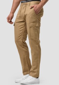 Pantalons cargo beiges avec une coupe droite, fabriqués en coton. Dotés de poches latérales et d'une ceinture élastique noire. Portez-les avec des baskets blanches.