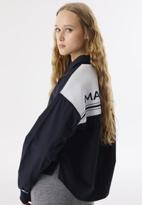 Giacca leggera blu navy con un accento bianco sulla spalla, caratterizzata da un tessuto testurizzato e un dettaglio ricamato "MA".