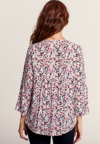 Blusa a fantasia floreale in azzurro chiaro, con maniche a campana lunghe. Il tessuto presenta forme astratte in rosa, nero e verde. Design a vita peplum.