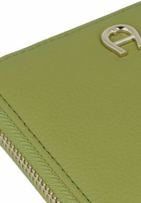 Portafoglio in ecopelle verde con logo metallico, dotato di chiusura a zip e superficie testurizzata. Dettaglio delle rifiniture lungo le cuciture.