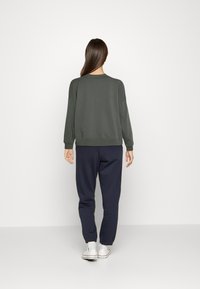 Mörkgrön sweatshirt med ribbade muddar och fåll, kombinerad med marinblå joggers. Enkelt mönster, tyg med en slät yta, bärs med vita sneakers.