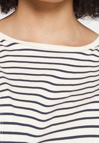Pruhovaný top s vodorovnými námořnickými pruhy na smetanovém pozadí, zaobleným výstřihem a měkkou, lehkou texturou látky.