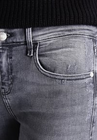 Jeans de denim gris con un corte ajustado, que presentan un clásico diseño de cinco bolsillos y un leve desgaste en la tela.