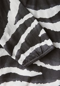 Sort og hvidt stof med dristige, abstrakte zebra-stribe mønstre. Glat tekstur med elastiske manchetter ved kanten.