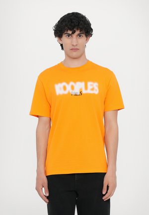 Orange cotton t-shirt with short sleeves, featuring a graphic print of "KOOPLES PARIS" in white and black. Simple crew neck design.