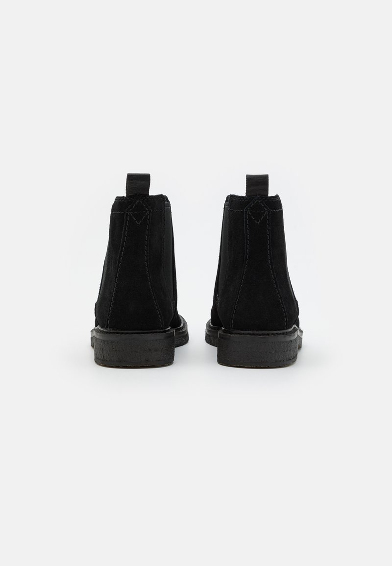 Bottines en suède noir avec un bout rond, semelle plate en caoutchouc noir et languette à l'arrière. Détails de couture verticale sur les côtés.