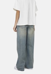 Jeans a gamba larga di colore azzurro chiaro, realizzati in denim, con una finitura sbiadita e due tasche posteriori. Abbinati a una maglietta bianca dalla vestibilità ampia.