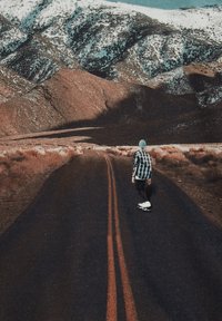 Skateboarder u kariranoj košulji vozi po tamnom asfaltu s dvije paralelne narančaste pruge, okružen planinskim područjem i snijegom.