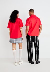 Červené tričká s krátkym rukávom na dvoch modeloch. Jeden má na sebe károvanú sukňu; druhý má čierne nohavice s bielymi vlnkovými pruhmi. Obaja majú na sebe biele ponožky.