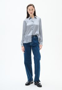 Randig blå och vit skjorta med knäppning fram, ihop med höga mörkblå jeans. Modellen har på sig svarta loafers.