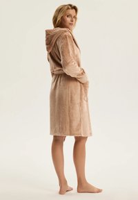 Beżowy szlafrok z kapturem wykonany z miękkiej, teksturowanej tkaniny; posiada wiązany pas, kieszenie oraz długość do kolan.